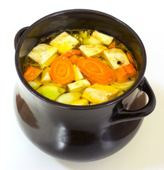 Clear Chicken broth with pieces of vegetables and spices in saucepan. Cooking chicken soup with vegetables in large clay black pot. 