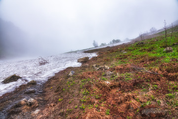 The last snow of winter melts on the hillside high in the mountains against the heavy fog. Contrast...