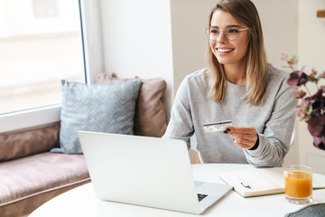 Photo of smiling woman using laptop while holding credit card