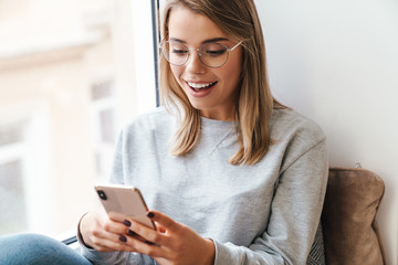 Photo of excited woman using smartphone while sitting near window