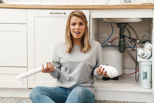 Photo of displeased woman with plumbing pipes while sitting on floor
