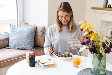 Obraz na płótnie Canvas Photo of cheerful young woman eating cereal while having breakfast