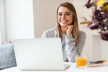 Photo of cheerful young woman using laptop while having breakfast