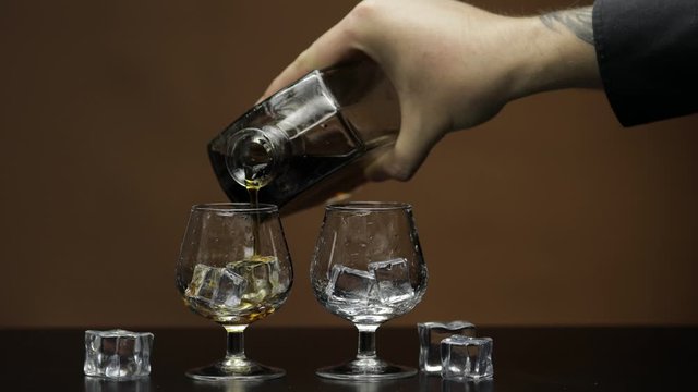 Pouring whiskey, cognac into glass. Brown background. Pour of alcohol drink