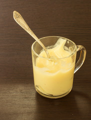 Custard vanilla cream in a glass cup. Jar of homemade curd with silver spoon over dark texture background. Homemade cream, vanilla pudding