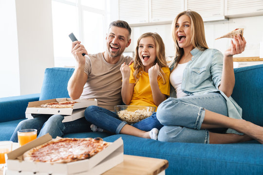 Photo of excited family eating popcorn and pizza while watching tv