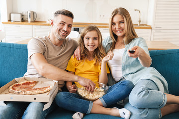 Photo of cheerful family eating popcorn and pizza while watching tv