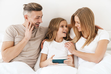 Photo of girl playing video game on cellphone with parents in bad