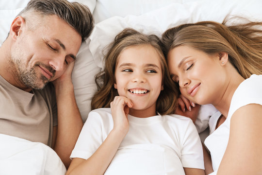 Photo of girl laughing while lying with sleeping parents
