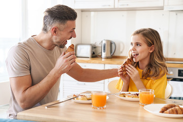 Obraz na płótnie Canvas Photo of father and daughter laughing while having breakfast in kitchen