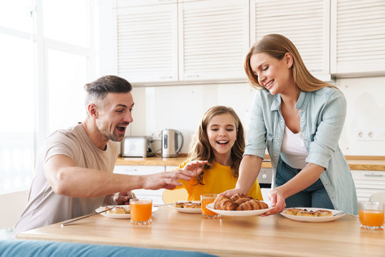 Photo of happy family eating croissants while having breakfast