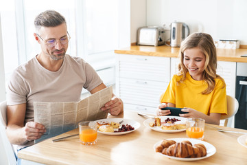 Photo of funny father and daughter using cellphone and reading newspaper - Powered by Adobe