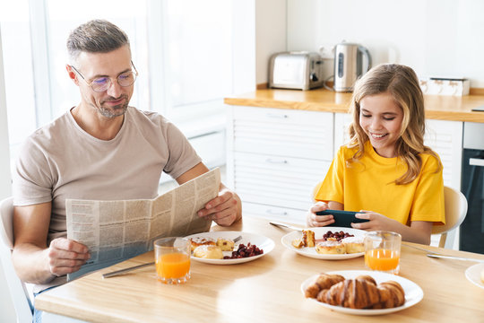 Photo of funny father and daughter using cellphone and reading newspaper