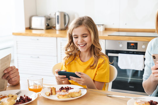 Photo of girl playing video game while having breakfast with her family
