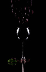 Red wine flows from the silhouette of a grape brush into a glass. The juice of the grapes is...