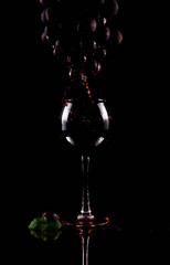 Red wine flows from the silhouette of a grape brush into a glass. The juice of the grapes is...