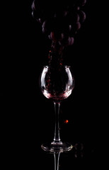Naklejka na ściany i meble Red wine flows from the silhouette of a grape brush into a glass. The juice of the grapes is squeezed out and flows into the glass.