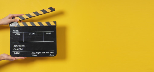 Hand is holding clapper board or movie slate.It is used in video production and film industry on yellow background. - obrazy, fototapety, plakaty