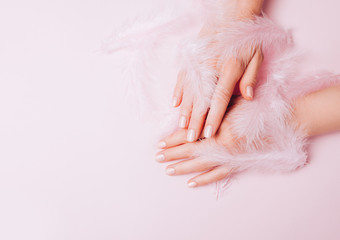 Stylish trendy female manicure. Woman's Hands holding pink pure feathers on pink background. Top view, flat lay.