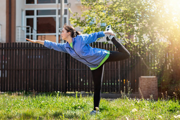 A young woman in sportswear performs an asana while doing yoga in her yard, on the grass. Outdoor....