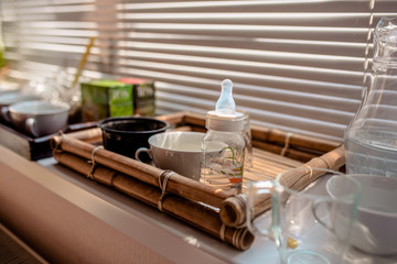 cups and a bottle for children standing on a bamboo tray on a window sill by the window