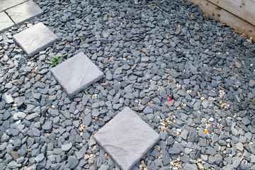 Grey aggregate and small textured rocks/stones with square textured block paving slabs irregularly...