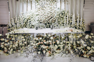 
wedding interior in a restaurant with flower decorations, glass countertops and large chandeliers. Tables decorated with white roses and long candles