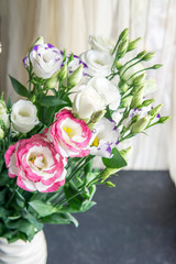 Bouquet of white, purple and pink eustoma flowers in white vase, dark table near window. Copy space. Flat lay of Valentines Day, Mothers Day, birthday celebration concept. Greeting card.
