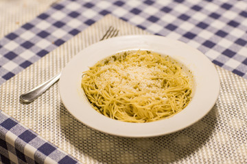 pasta with cheese and herbs in a white plate and a fork on a wooden stand