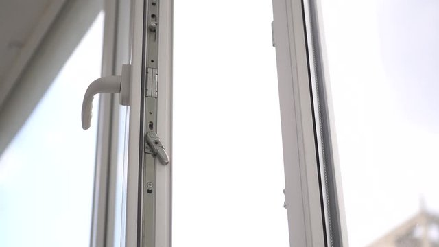 The woman opens and closes a white plastic window by the handle .