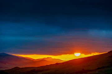 Fototapeta na wymiar Sun setting over Silhouetted Mountains, Clouds 