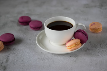 White cup with black coffee and bright macaroon cakes on a concrete background.