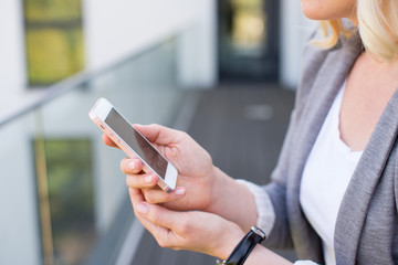 Mockup blonde woman watching her smartphone with empty screen in a modern building. Real Estate Agent with mockup smartphone. Young woman with phone in green background