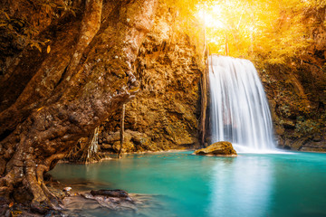 Fototapeta na wymiar Waterfall and blue emerald water in autumn forest with sun flare and sunlight in morning. Erawan Waterfall step 3rd. Beautiful nature rock waterfall steps in rainforest at Kanchanaburi, Thailand