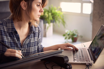 Young woman working from home due to the global pandemic. Illustrator working on the drawing tablet in her living room