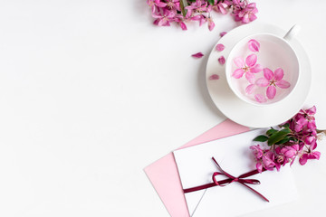 Spring background for the inscription, pink flowers, sakura cherry blossoms, letters, a cup with water and flower petals, top view, circle frame, copy space, flat lay 