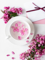 Obraz na płótnie Canvas Spring background for the inscription, pink flowers, sakura cherry blossoms, letters, a cup with water and flower petals, top view, frame, copy space flat lay 