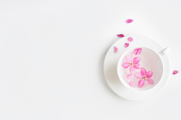 Spring background for the inscription, pink flowers, sakura cherry blossoms, cup with water and flower petals, fashion trend of the year, top view, creative banner, copy space flat lay
