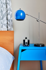 a modern bedroom with a side table, lamp, and vintage camera