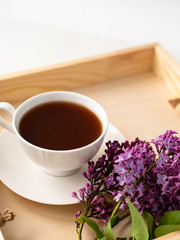  porcelain cup with coffee, cocoa, spring breakfast on a wooden tray. Branches and flowers of lilac, violet color, on a white background. Minimalistic design