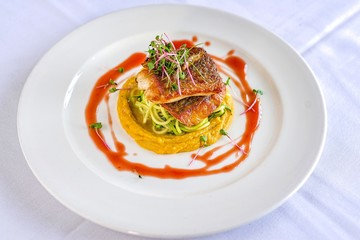 Stacked grilled salmon with onion rings salad, vegetable, and sauce on white plate