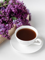 Obraz na płótnie Canvas porcelain cup with coffee, cocoa, spring breakfast on a wooden tray. Branches and flowers of lilac, violet color, on a white background. Minimalistic design