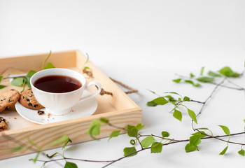 Cup with coffee, cocoa, chocolate chip cookies, spring breakfast on a wooden tray. Branches with leaves, greenery, on a white background. Minimalistic design, creative banner, with copy space