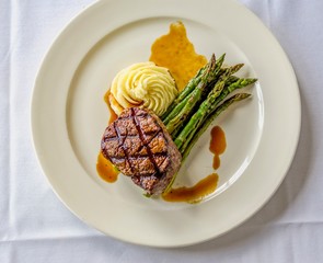 Grilled rib eye steak with creamy mashed potatoes, grilled asparagus, and au jus sauce on white...