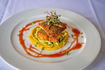 Stacked grilled salmon with onion rings salad, vegetable, and sauce on white plate