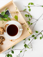 A cup of coffee, tea, chocolate chip cookies, a meal on a wooden tray. Branches with leaves, greenery, on a white background. Unity with nature.Minimalistic design, creative banner,flat lay, top view
