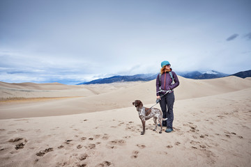 a young woman and her dog hiking among sand dunes