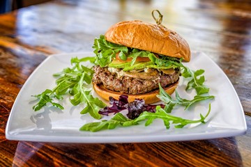 Gourmet grilled hamburger on bun with mushrooms, avocado, arugula, radicchio and white plate.