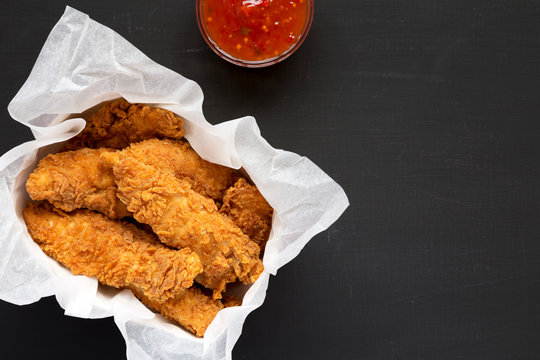 Homemade chicken tenders with sour-sweet sauce on a black background, top view. Flat lay, overhead, from above. Space for text.