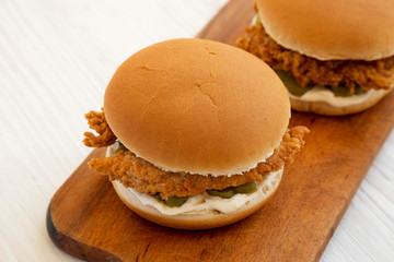 Homemade Burgers with fried chicken strips on a rustic wooden board on a white wooden table, low angle view. Close-up.